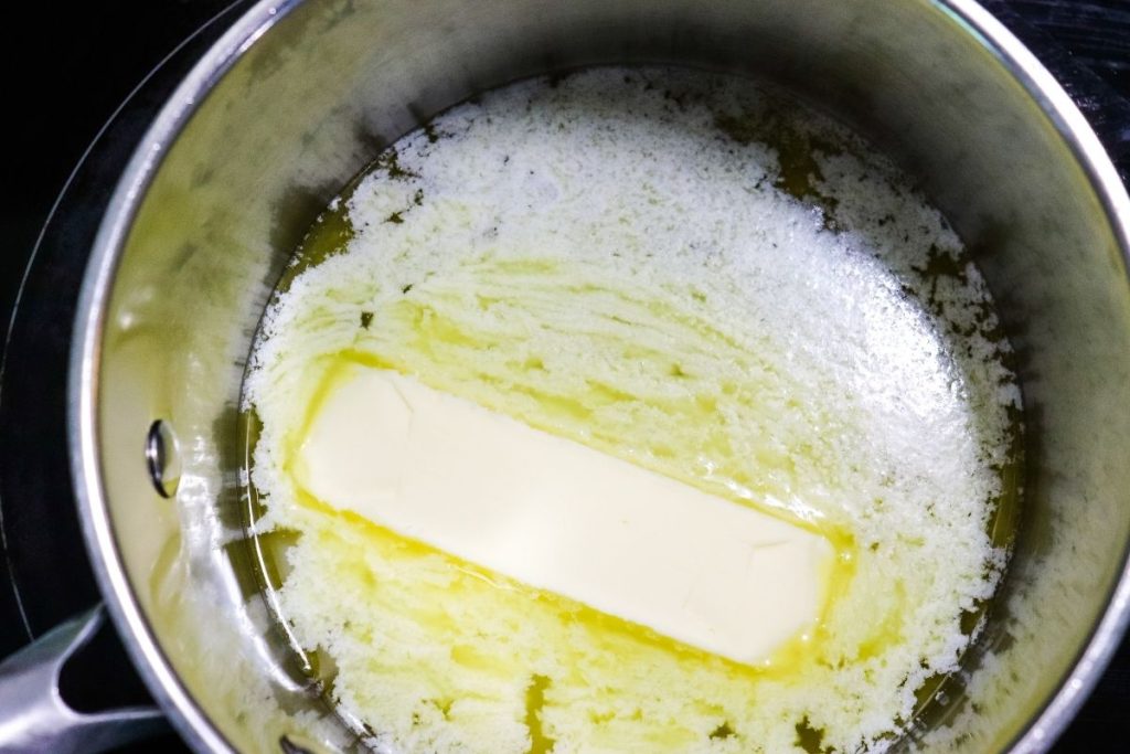 A stick of butter melting in a stainless steel saucepan on a stovetop.