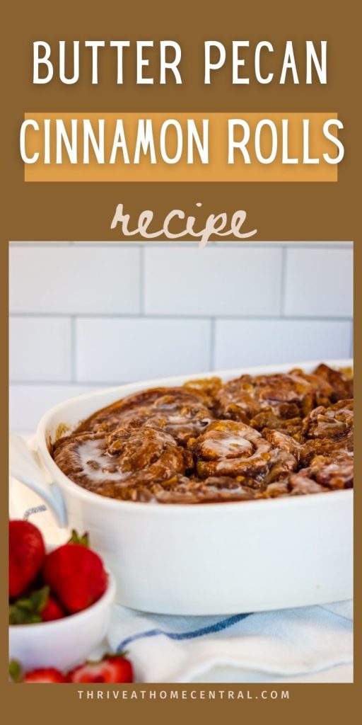 A white baking dish filled with butter pecan cinnamon rolls sits on a counter, with strawberries and a blue-striped towel nearby. Text overlay reads "Butter Pecan Cinnamon Rolls Recipe.