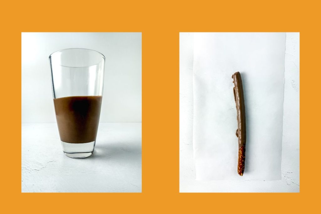A glass half-filled with chocolate milk sits on the left, while a single chocolate-covered pretzel stick lies on parchment paper to the right, both on a white background with an orange border.
