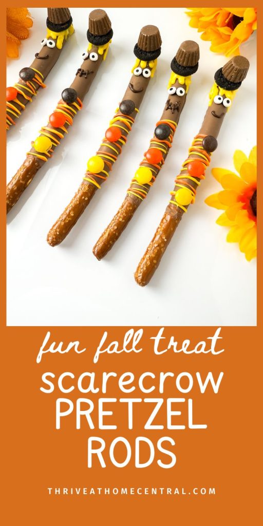 Five pretzel rods decorated as scarecrows with candy, icing, and small candies arranged on a white surface with artificial sunflowers.