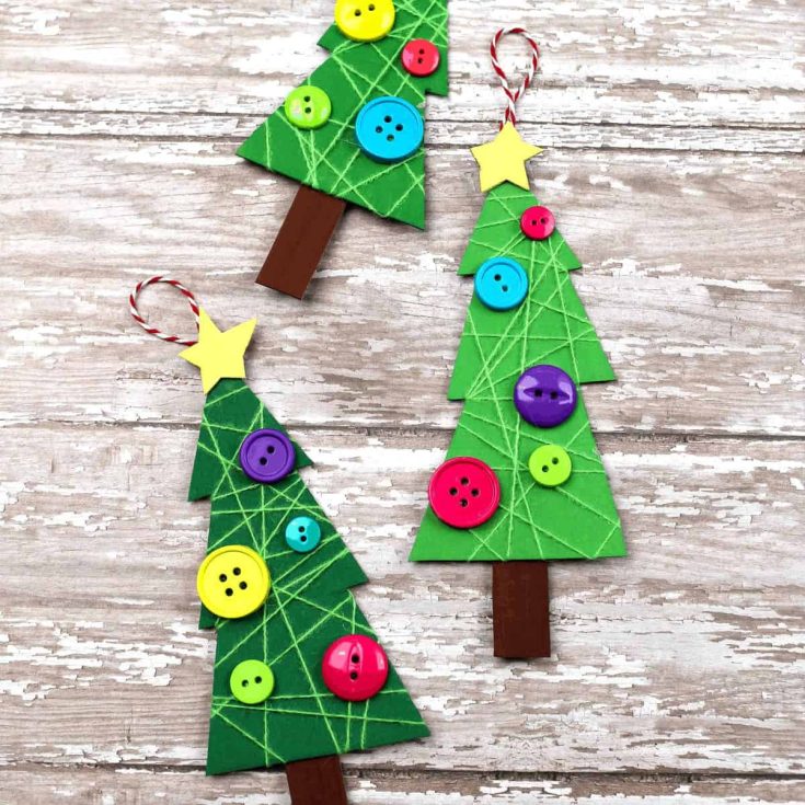 Three handmade Christmas tree ornaments made from green cardboard, decorated with colorful buttons, yellow star toppers, and red-and-white string loops, on a wooden surface.